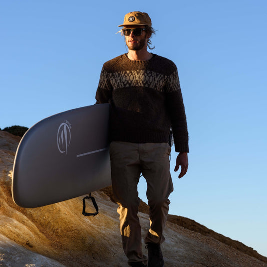 Surfista con tabla evolutiva caminando por la playa al atardecer, equipo técnico de surf
