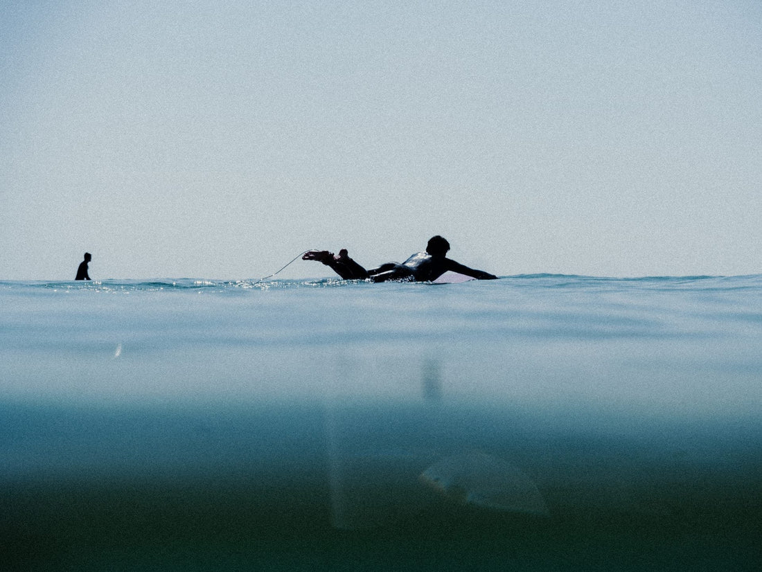 Surfista remando sobre su tabla en aguas frías, técnica de remada en olas de invierno.