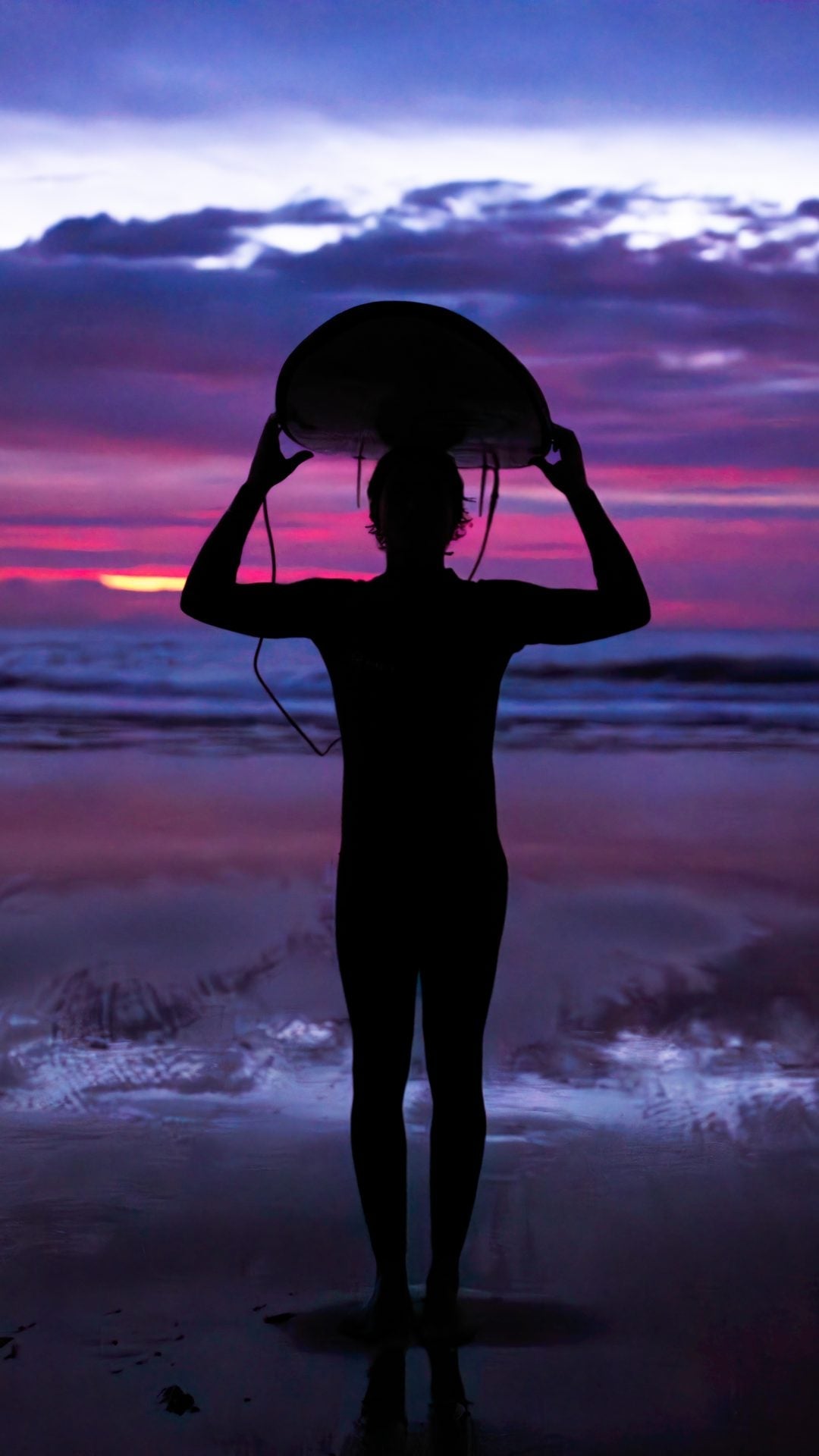 Surfista al atardecer sosteniendo su tabla frente al mar y pensando en la Recuperación después de surfear