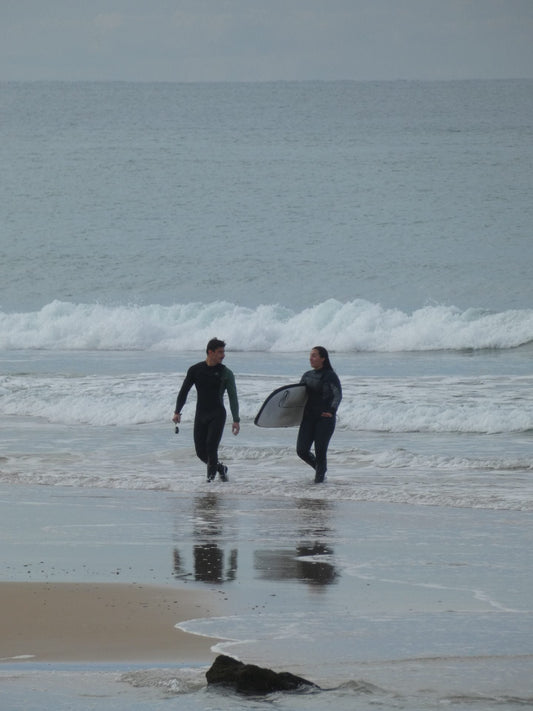 Dos surfistas con traje de neopreno caminando por la orilla en un día nublado tras surfear