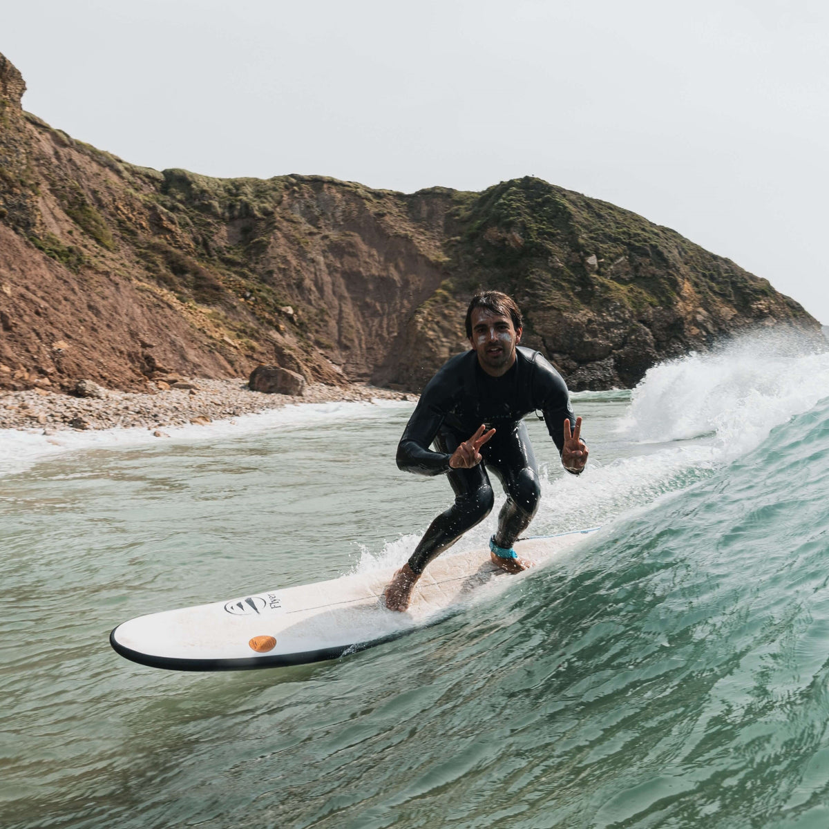 Surfista en tabla evolutiva disfrutando una ola en playa rocosa, material técnico de surf