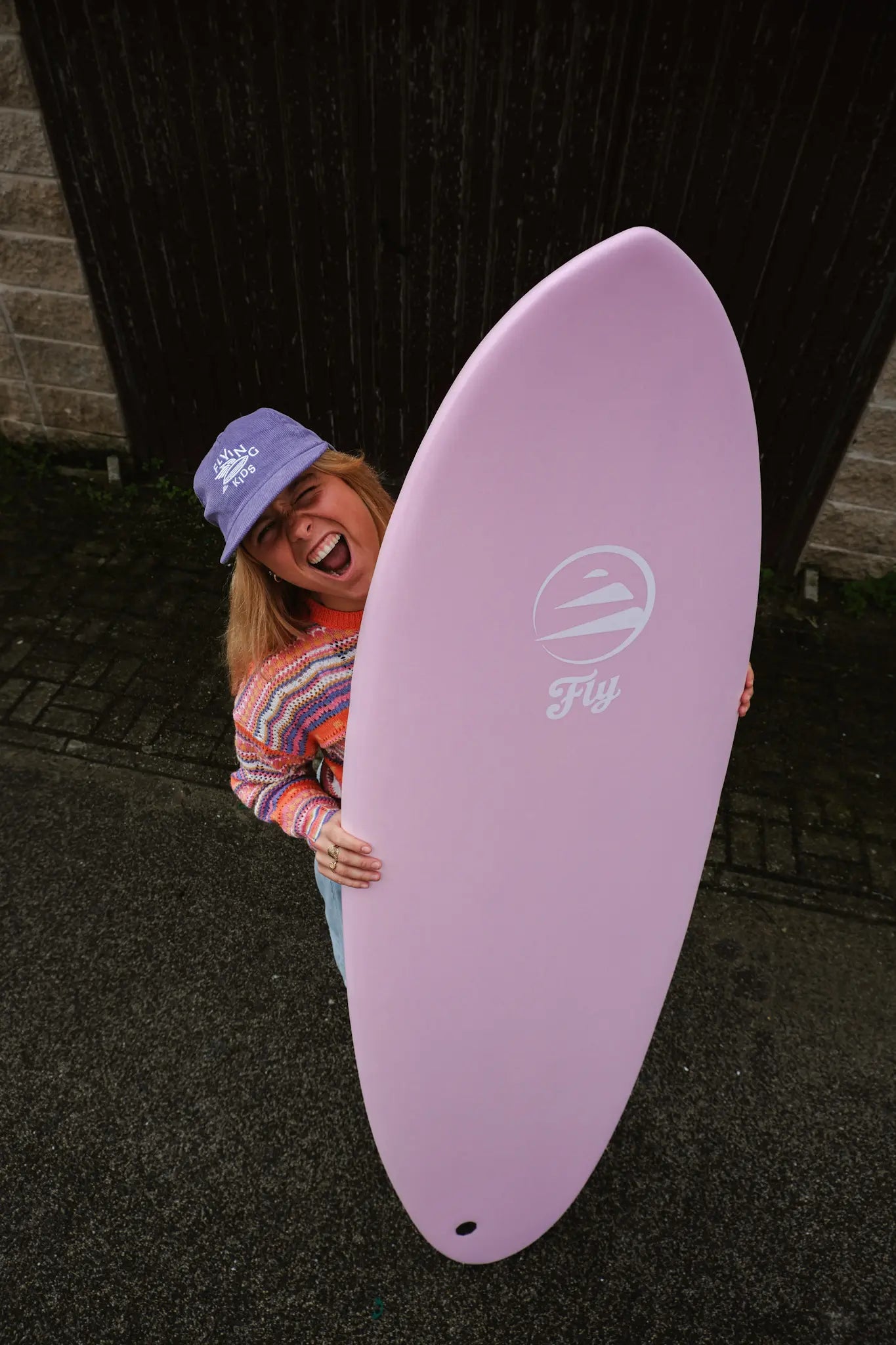 Chica sonriendo enseñando la tabla de surf de corcho rosa para tus sesiones de surf.