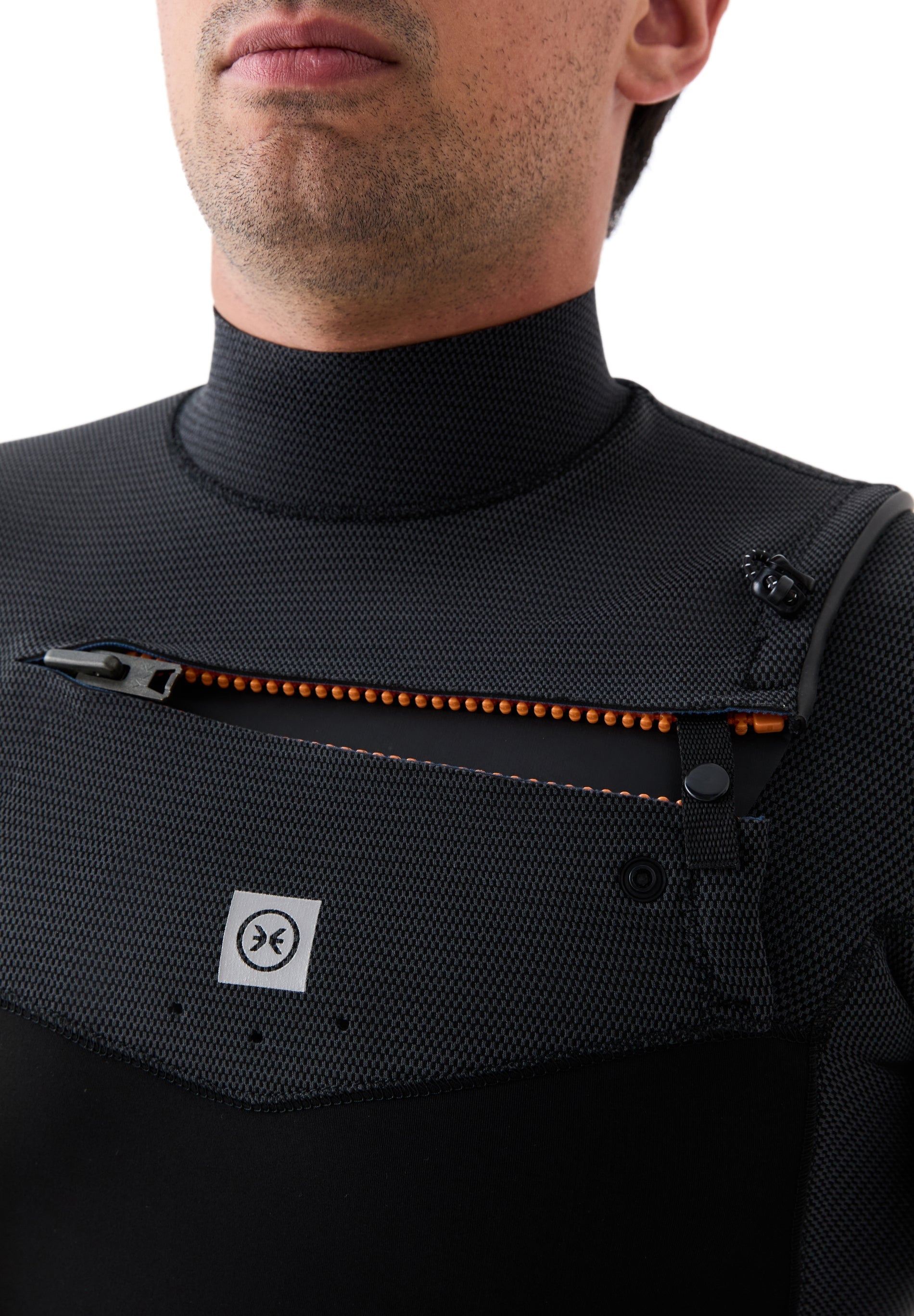Detalle de la cremallera en el pecho (chest zip) con tirador naranja, diseñada para facilitar la entrada y mejorar la estanqueidad.