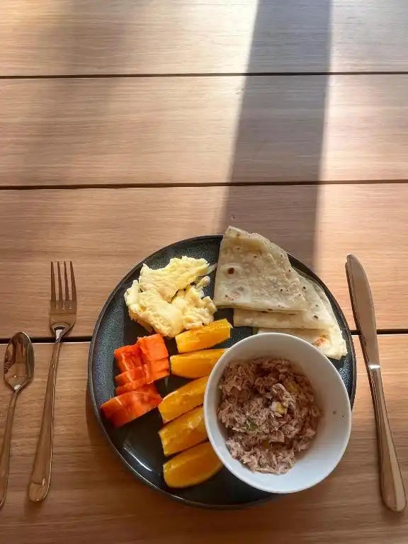Plato de frutas tropicales frescas y café servido en una mesa de madera al aire libre.