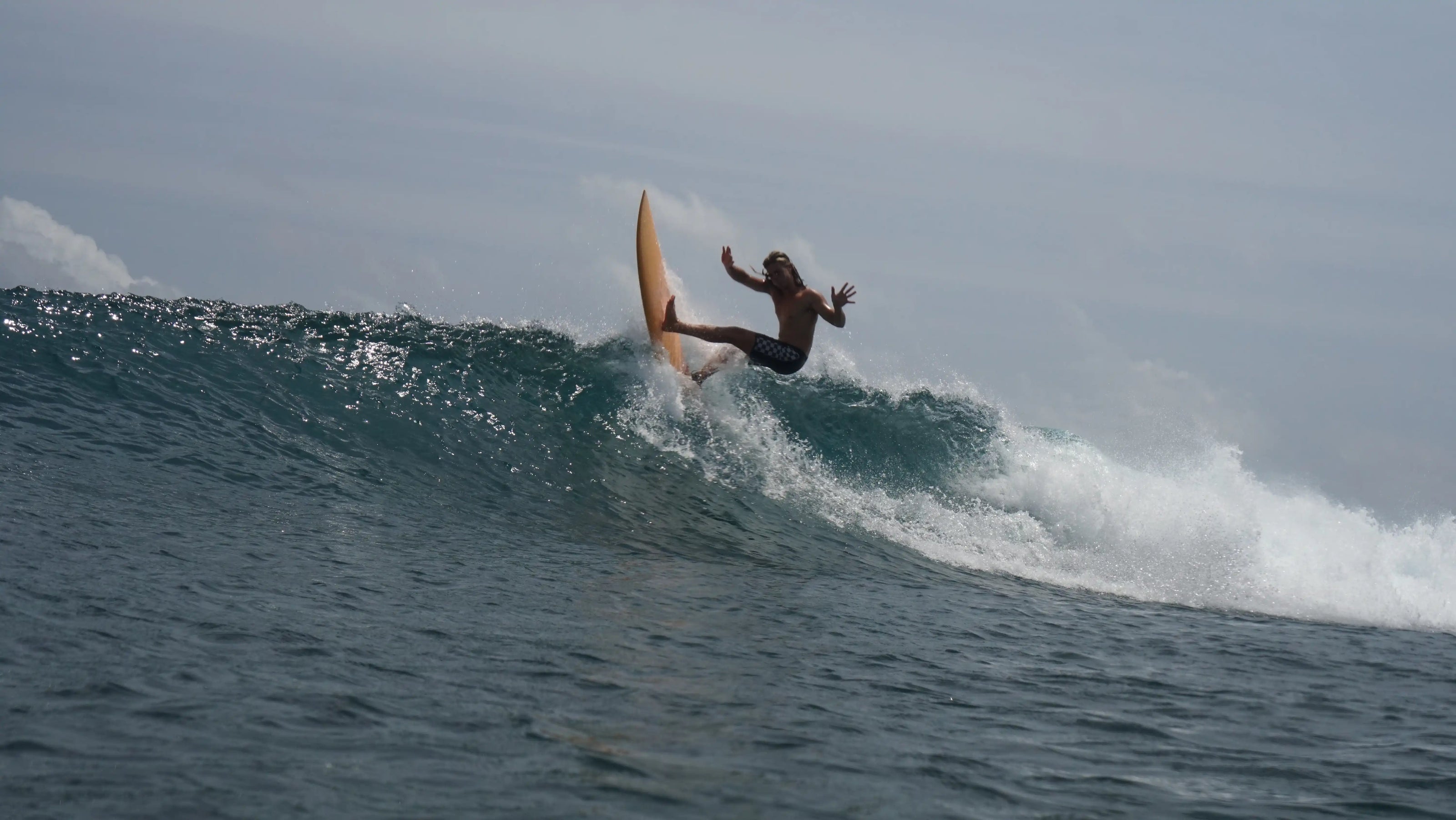 Surfista realizando un giro en la parte superior de una ola transparente en Maldivas.