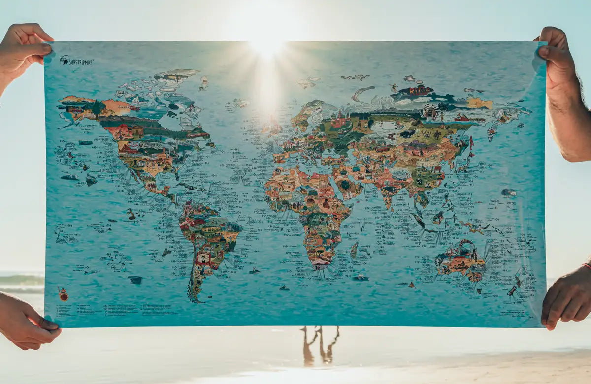 Mapa de surf del mundo ilustrado a mano sujetado en la playa al atardecer