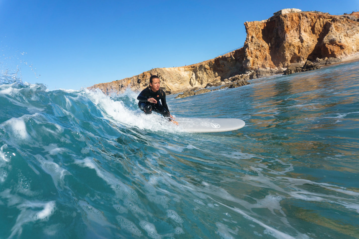 Mujer surfeando una ola en un día soleado con una tabla de surf epoxy de 7.6 pies