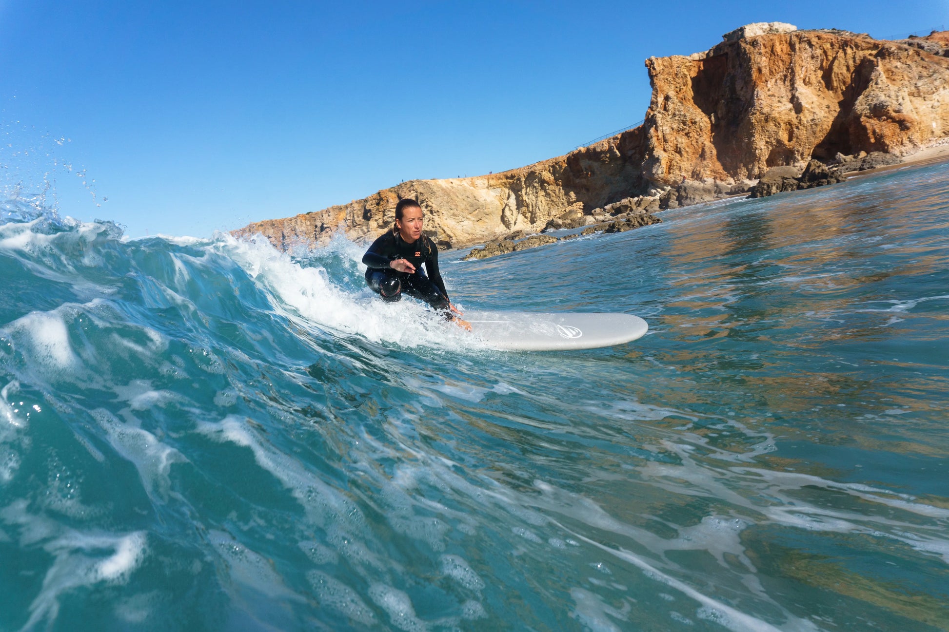 Mujer surfeando una ola en un día soleado con una tabla de surf epoxy de 7.6 pies