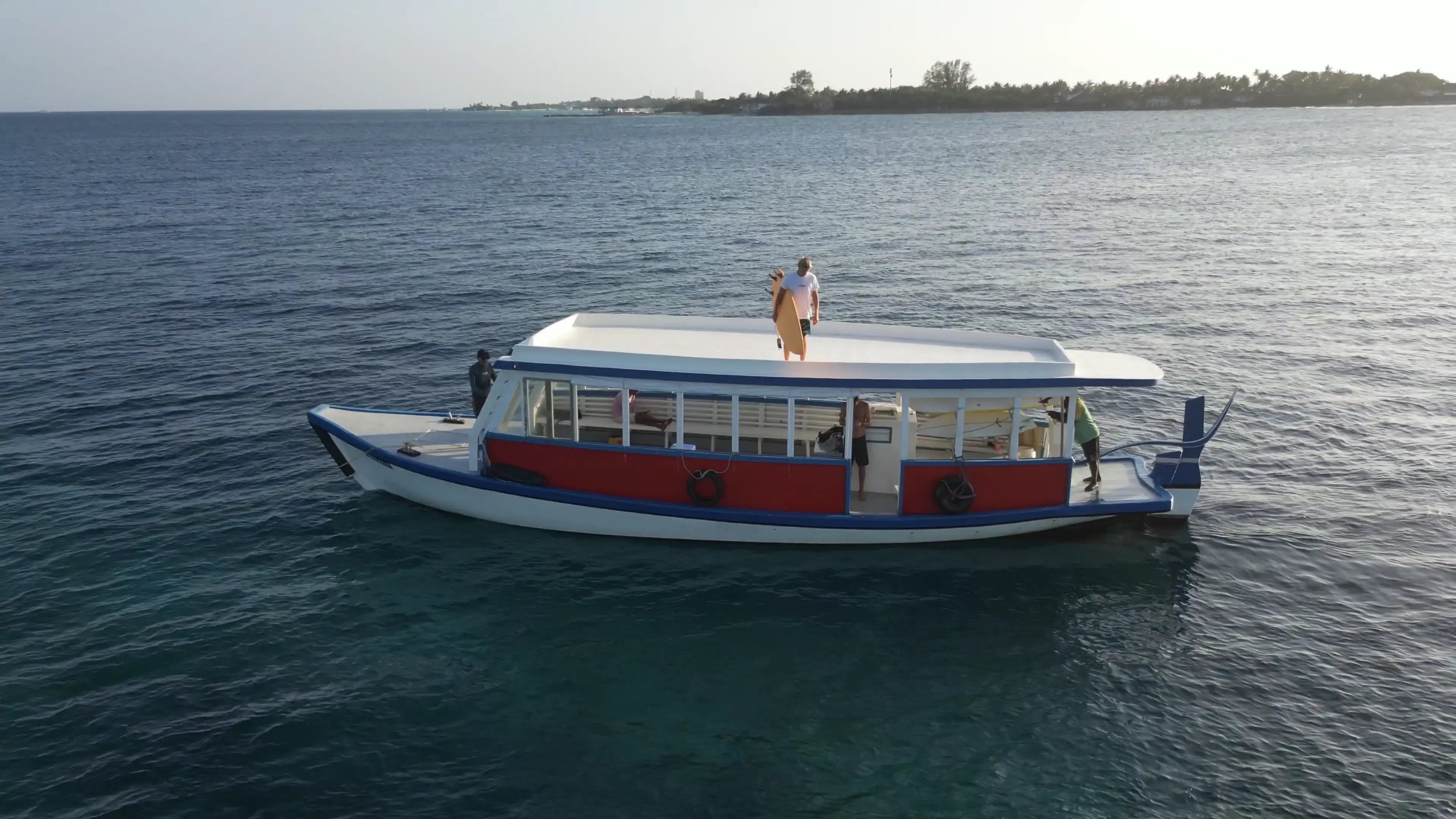 Surfista con su tabla sobre el techo de un barco tradicional dhoni en el mar.