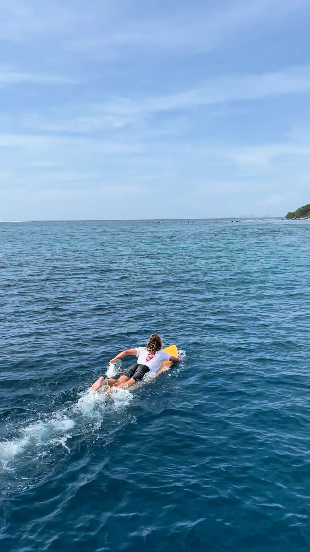 Surfista remando hacia el line-up en una laguna azul turquesa en Maldivas.