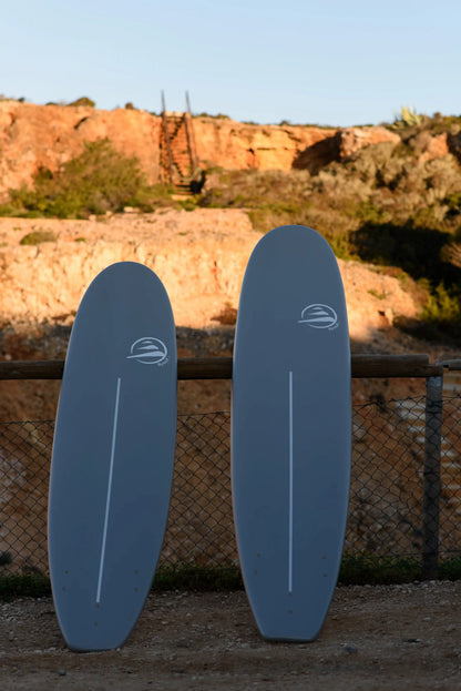 Dos tablas de surf de cool school epoxy apoyadas verticalmente contra una pared en un entorno costero.